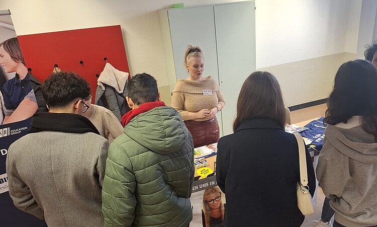 Interessierte Schülerinnen und Schüler stehen am Euro Akademie-Messestand und lassen sich von der Mitarbeiterin informieren und beraten.