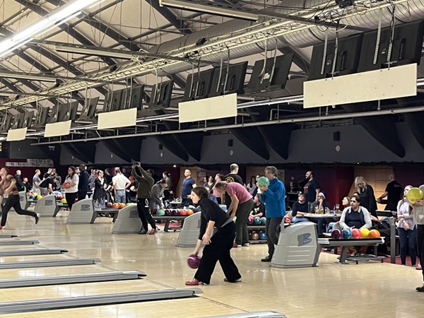 Große Halle mit vielen Bowlingbahnen und den spielenden Mitarbeitenden.