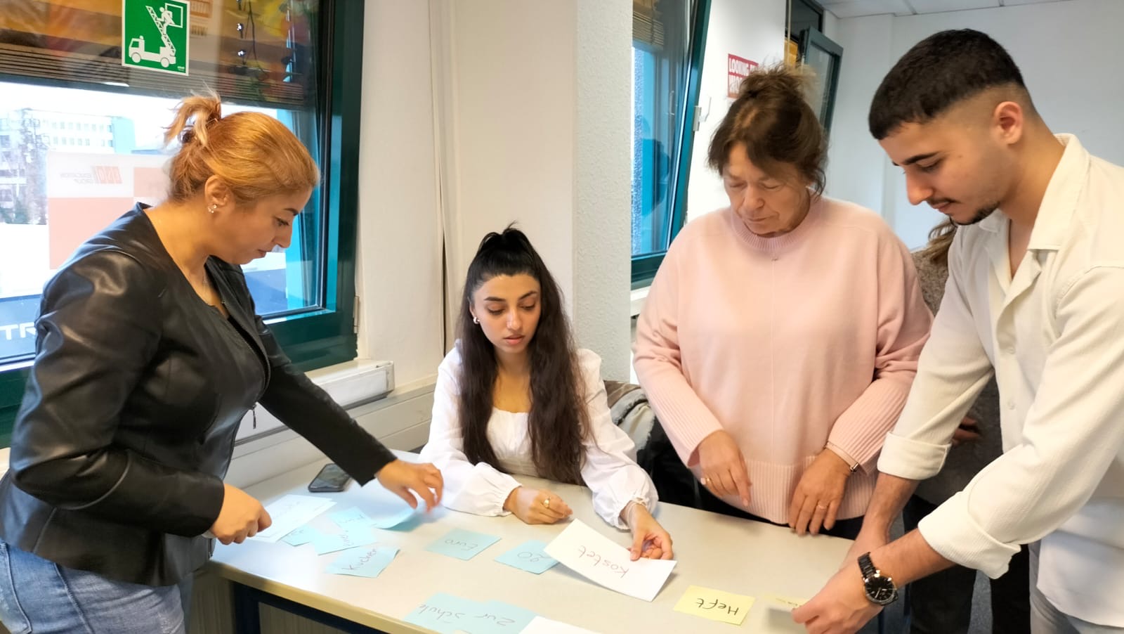 Vier Kursteilnehmende betrachten eine Aufgabe, die in Form von Zetteln auf einem Tisch liegt.